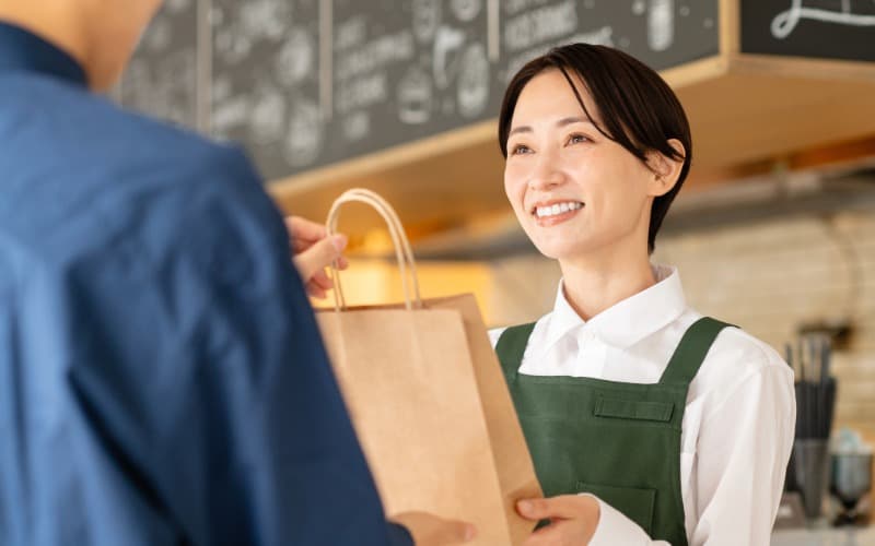 カフェの女性店員がお客様に商品の入った紙袋を受け渡す