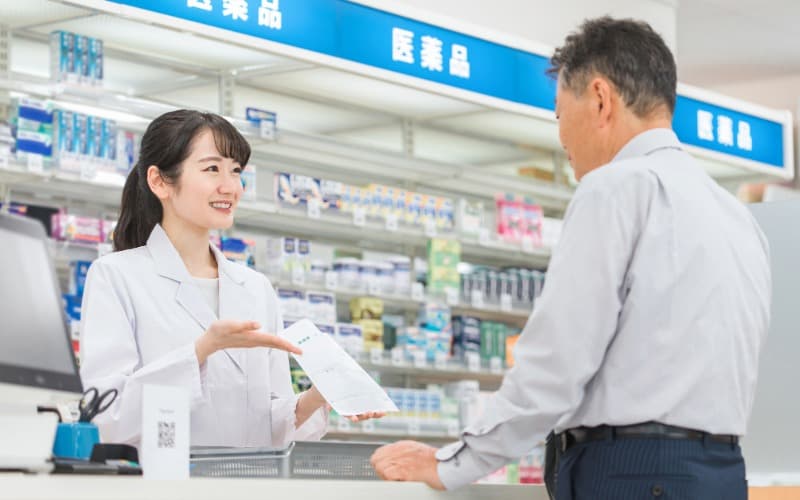 薬局のレジで高齢男性のお客様に薬の説明をする女性薬剤師